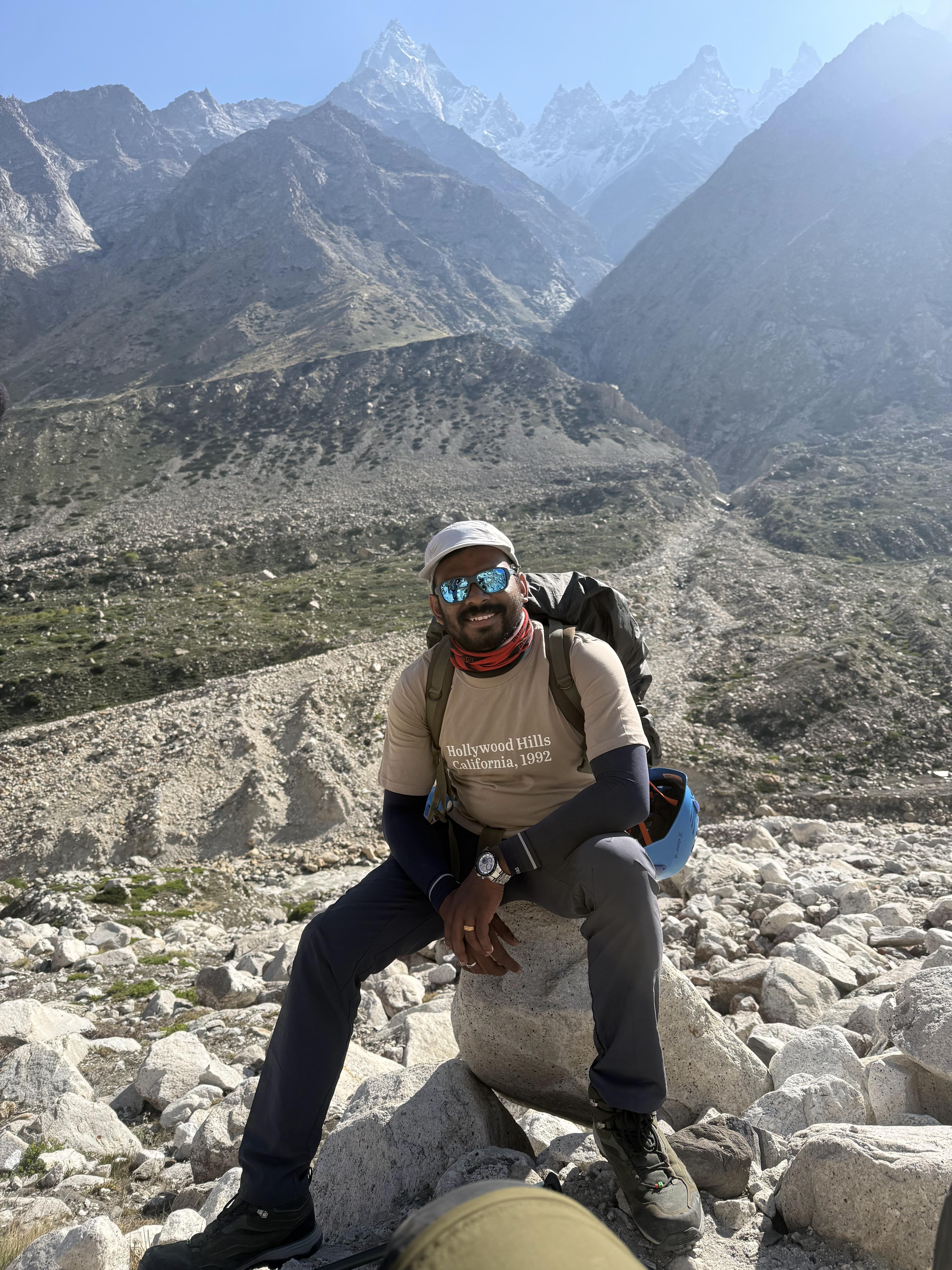 Vairav sitting on a boulder during a high-altitude trek, snow-capped mountain peaks in the background.