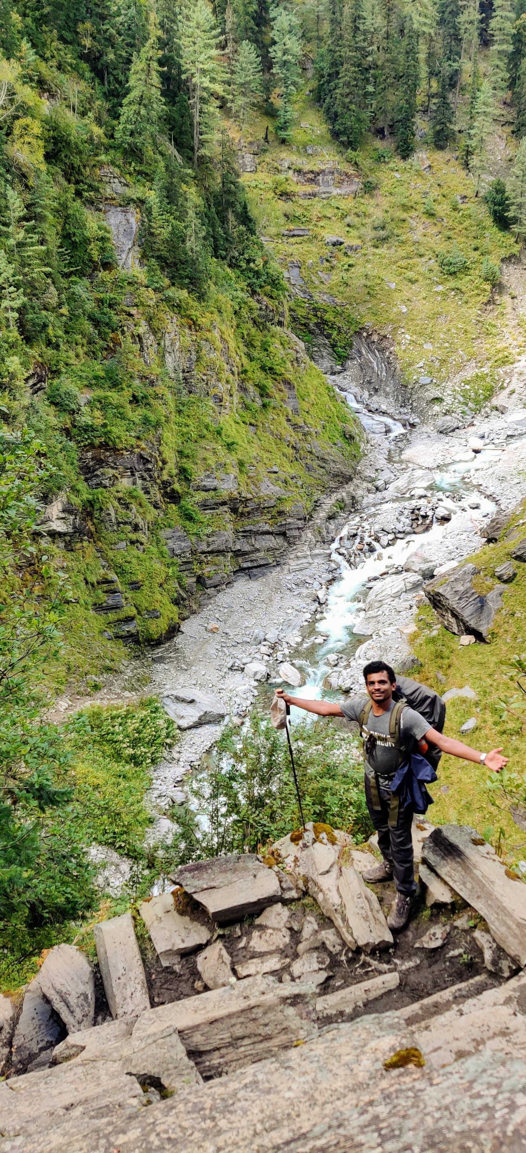 Vairav standing on a rocky ledge above a forested gorge with a river running through the valley below.